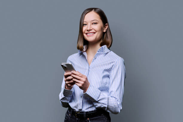 istock Young smiling woman using smartphone looking at camera in grey background 2188925679