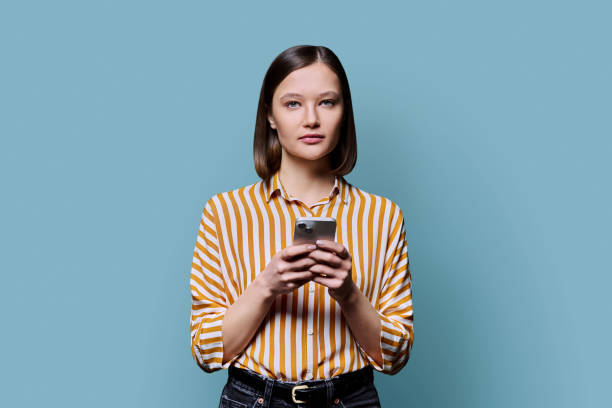 istock Young serious woman using smartphone looking at camera in blue background 2188925703
