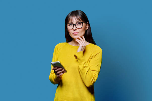 istock Middle aged beautiful woman holding smartphone looking at camera on blue background 2188925894