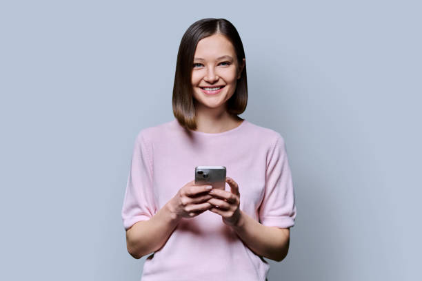 istock Young smiling woman using smartphone looking at camera in grey background 2188926016