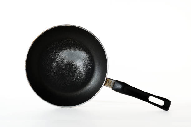 An old, round, scratched frying pan sits on a white background. This essential kitchen tool is ready for a variety of cooking tasks.