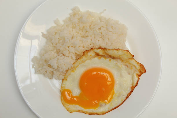 Sunny side up or fried egg with rice on white plate. Runny, liquid and broken egg yolk