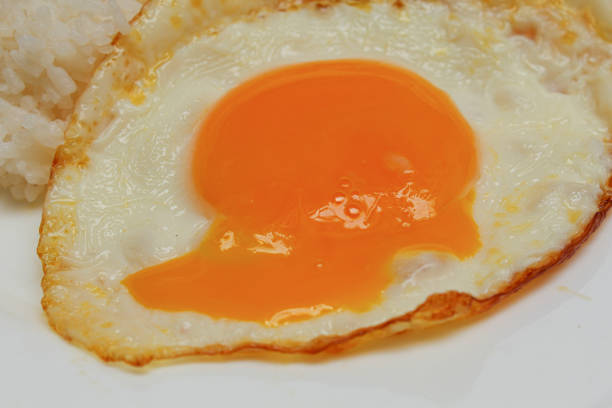 Sunny side up or fried egg with rice on white plate. Runny, liquid and broken egg yolk