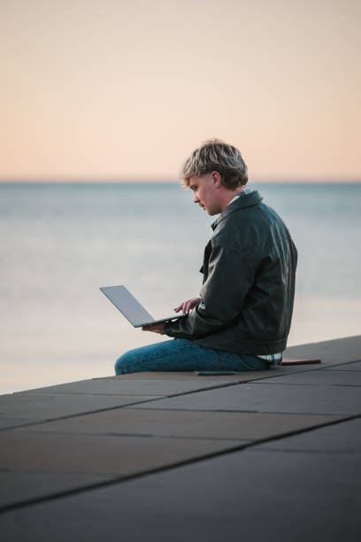 istock Man working on laptop by water at sunset 2188931336