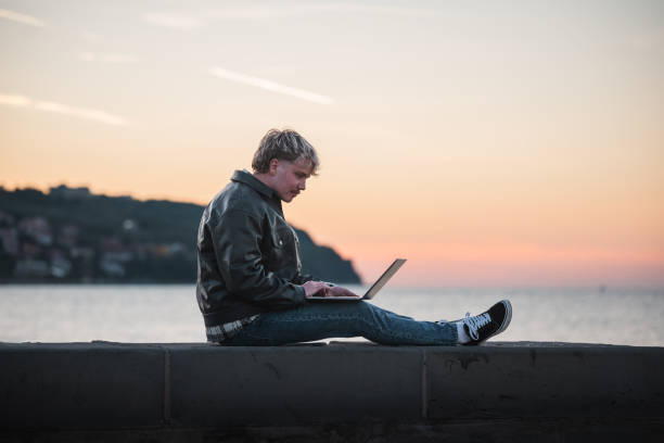 istock Man working on laptop by the sea during sunset 2188931366
