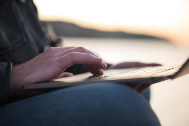 istock Man typing on laptop by water's edge during sunset 2188931373