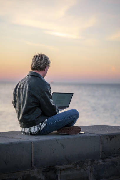 istock Man working on laptop by the ocean at sunset 2188931376