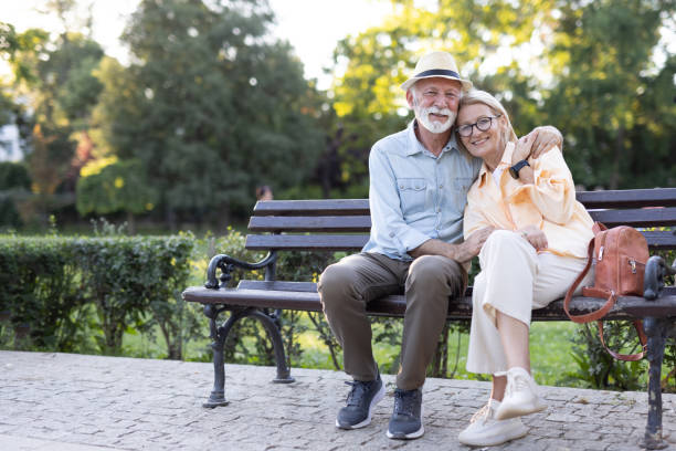 istock Elderly couple smiling on bench in park with serene background 2188932479