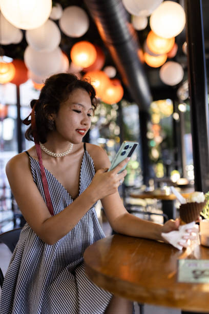 istock Woman enjoying a moment in a cozy cafe with colorful lanterns while using her smartphone and holding an ice cream cone in a relaxing setting. 2188935548