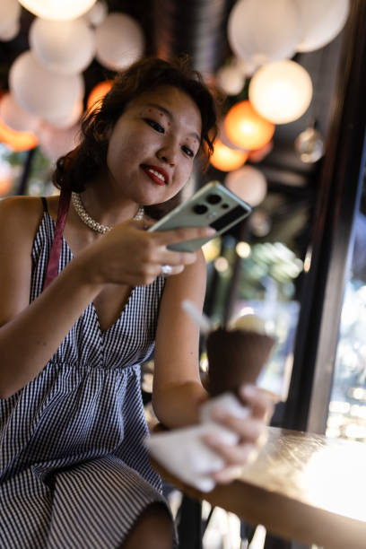 istock Smiling young woman enjoying ice cream while using smartphone in a lively cafe with glowing lights 2188935567