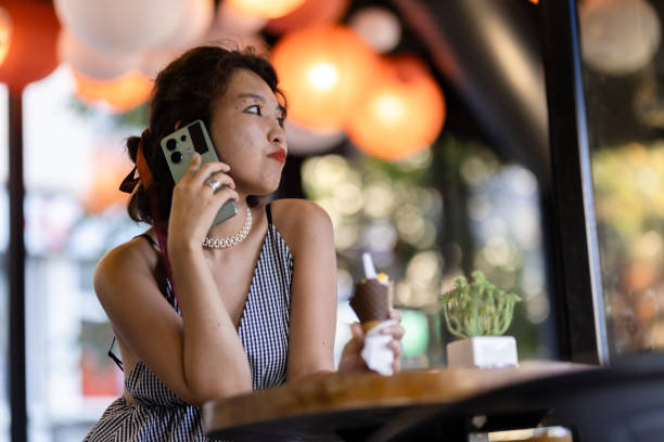 istock Woman enjoying ice cream while talking on smartphone in a decorated cafe with warm lighting and vibrant ambiance 2188935599
