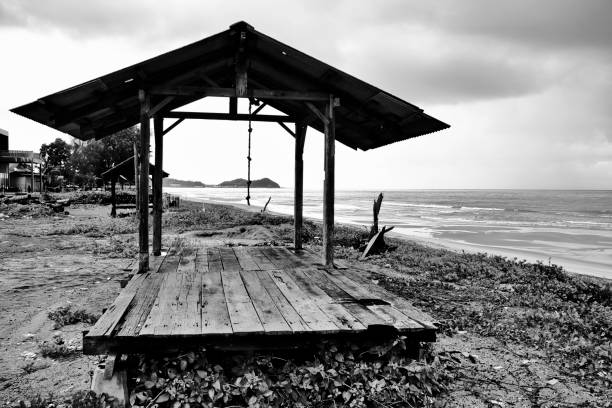 A wooden gazebo, in contrast to the dark waves and the bright sky, is picturesque in black and white, creating a dramatic and atmospheric scene that evokes a sense of solitude and introspection.