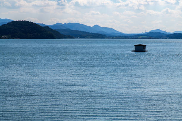 A floating platform for swimming is anchored in the calm waters of Chiemsee in Bavaria, Germany. The lake reflects the surrounding landscape and distant mountains under a colorful evening sky, capturing the peaceful atmosphere of summer in the Bavarian Alps.
