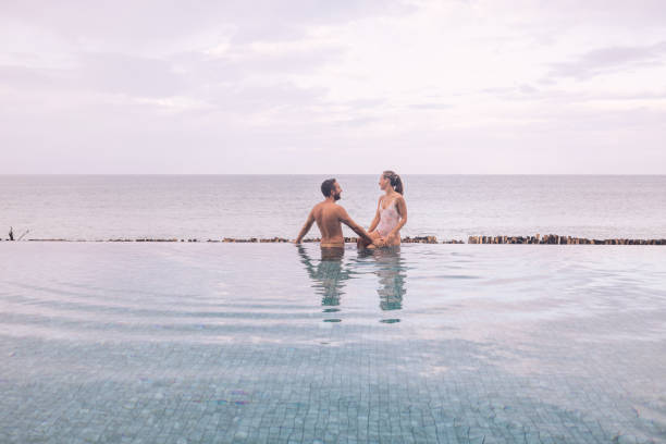 istock Couple Relaxing by Infinity Pool Overlooking Ocean 2188951696