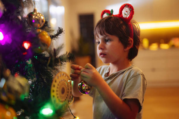 The young boy adds colorful ornaments to the Christmas tree