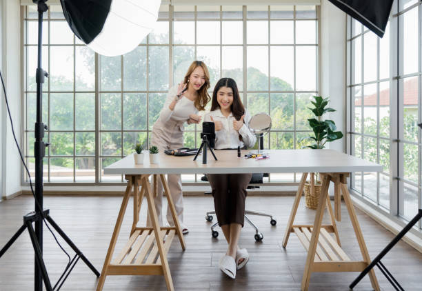 istock Two asian women creating content for social media. They are using a studio setup that include a smartphone mounted on a tripod, lighting equipment and various makeup products arrayed on the table. 2188970669