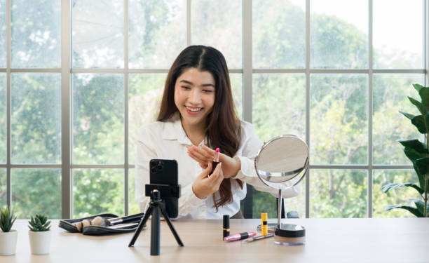 istock A woman filming her makeup tutorial in a bright room with large window, using a smartphone mounted on a tripod, various makeup product are on the table. 2188970672