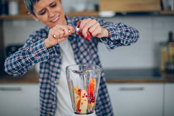 Unrecognisable child making fruit smoothie with blender. She is mixing fruits with blender. Fruits and blender are on kitchen counter.