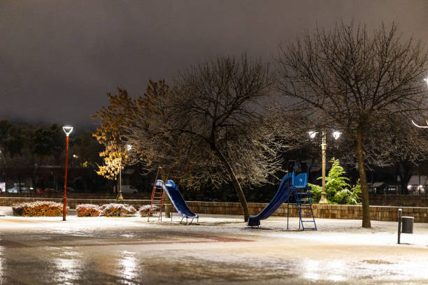 Empty playground in city park during snowy winter evening