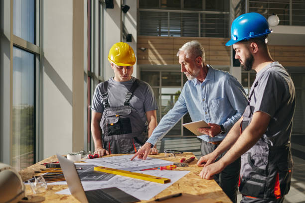 istock Inspector and manual workers reading blueprints in construction building. 2188977068