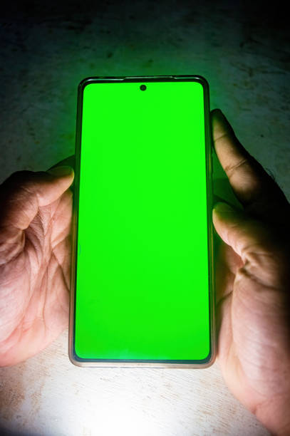 istock A person holding a smartphone with a bright green screen, possibly for chroma key or display testing purposes. The vibrant display stands out against the dimly lit background 2188977159