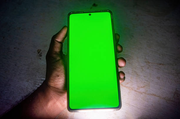 istock A hand holding a smartphone with a bright green screen, highlighting the device's display in a dimly lit environment. Ideal for technology and gadget related themes 2188977432