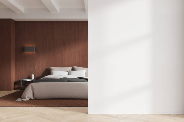 istock Modern bedroom with bed, pillows, and side table. Empty wall space on right for mockup. Wooden floor and paneling. 3D Rendering 2188980355