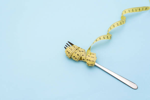 Fork Wrapped with Yellow Measuring Tape on a Blue Background: Diet and calories Control concept