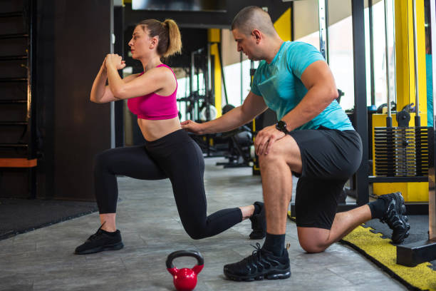 istock Young woman doing lunges with personal trainer at the gym 2188983335
