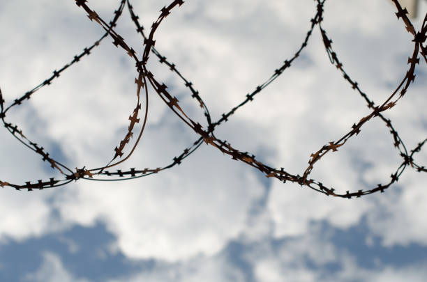 old rusty barbed wire fenced against the blue sky and white clouds