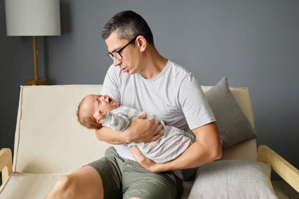 istock A father gently cradles his newborn baby while sitting on a light-colored sofa in a contemporary living room. The atmosphere is calm and loving, showcasing their bond 2188996145