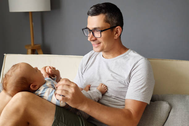 istock A father is laughing and playing with his infant child while sitting comfortably on a sofa. They share a joyful moment in a stylish living room adorned with soft lighting 2188996170