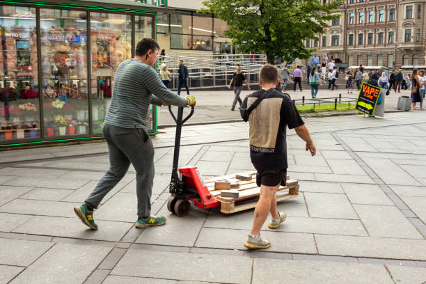 Saint-Petersburg, Russia - 2 August 2024. Two men are pushing a pallet on a cart. One man is wearing a black shirt and the other is wearing a gray shirt