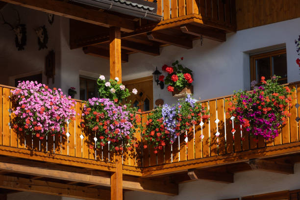 A lovely wooden balcony features colorful flowers in pots, adding charm to a stone building in Tirol, Austria. The scene captures the essence of rustic alpine living.