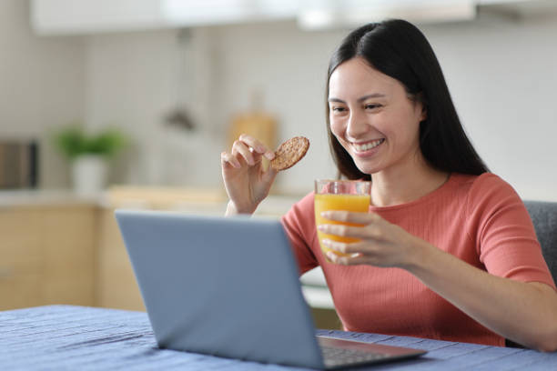 istock Happy asian woman eating and drinking using laptop 2189002631