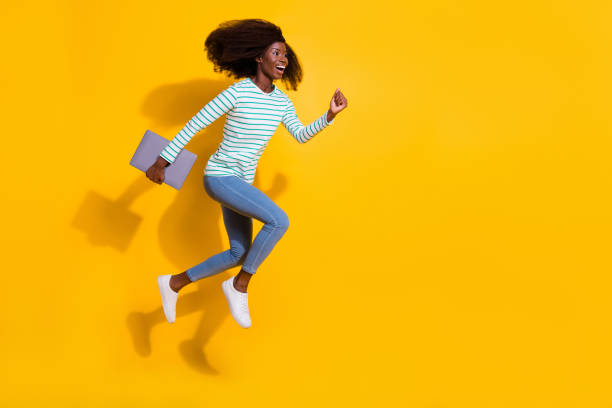 istock Full length profile portrait of active cheerful lady hold netbook jump rush empty space isolated on yellow color background 2189004936