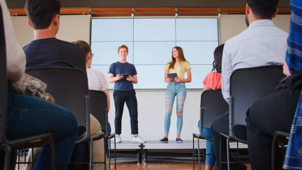 istock Two College Students Giving Presentation To High School Or University Class In Front Of Screen 2189009192