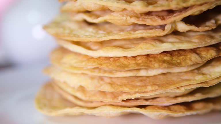 A stack of layers cakes for caramel cake on cooling rack. stack of cake layers spreads cream on the cake layers. Stacks layers one on top of the other. Nearby ingredients for making the cake