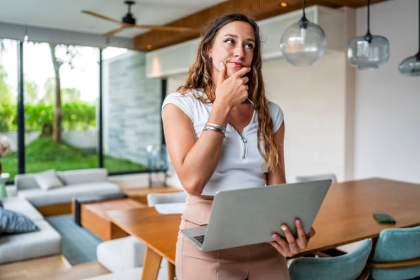 Thoughtful Woman Holding Laptop in Modern Home Office Setting