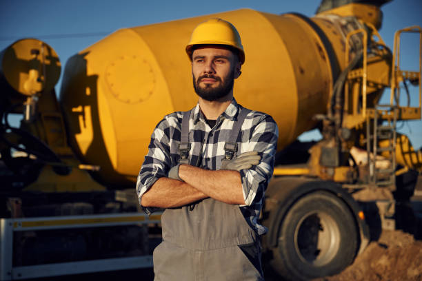 Yellow concrete mixer truck parked behind. Worker is on the construction site at daytime.