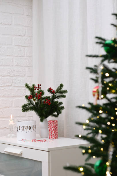 istock Festive and Cheerful Winter Decor Featuring a Candle Surrounded by Greenery on a White Table in front of Christmas tree. 2189019654