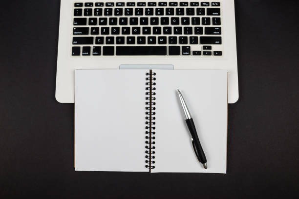 istock Top view of empty white notepad with pen and laptop on black background. copy space. 2189019937