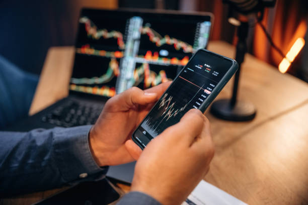 istock Close up view of trader's hands that holding phone with crypto data, laptop on the table 2189021767