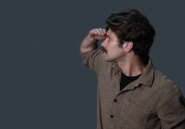 Man holding hand over eyes looking into distance, studio shot