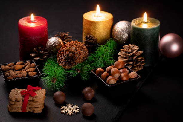 Festive Christmas table arrangement featuring glowing candles, sparkling garlands, pines cones, holiday sweets and assorted nuts.