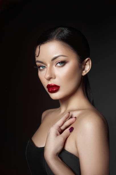 istock woman poses gracefully with striking red lips and flawless makeup, highlighting her features. Her sleek hair and elegant attire create a captivating visual contrast against the dark background 2189032278