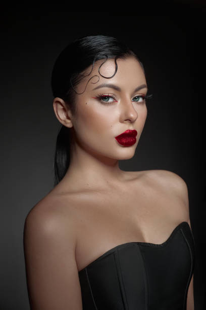 istock woman poses confidently with dramatic makeup featuring bold red lips and defined eyelashes. Her sleek hairstyle adds to the overall elegance in a softly lit, dark atmosphere 2189032302