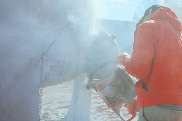 Worker skillfully operates concrete saw, cutting through drainage system well while dust fills air at construction site