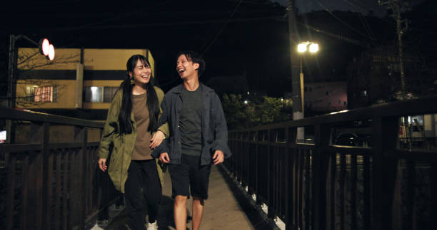 istock Bridge, couple and happy at night with walking for bonding, exercise routine and fun in Japan. People, relationship and smile or laugh outdoor with funny conversation, joke and comedy on break 2189035248