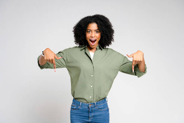 istock An exultant African-American woman with a wide grin points down with both hands towards an imaginary product 2189036344